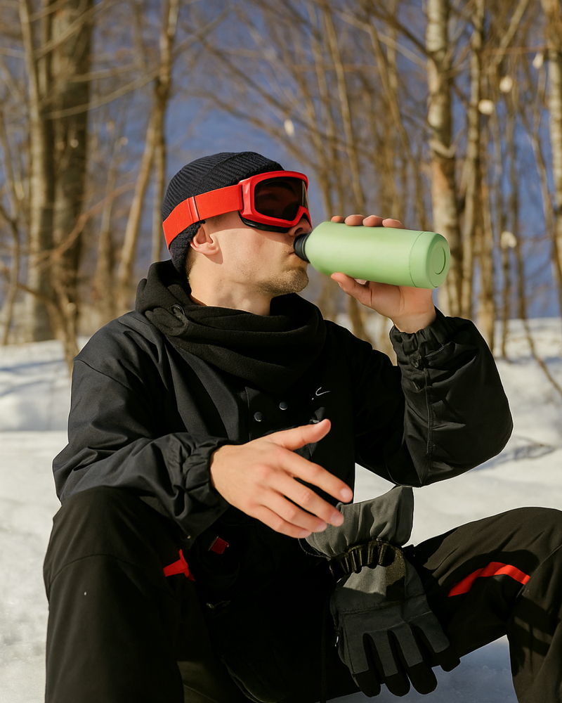 Man in wintersportkleding drinkt uit een groene Vireau RVS thermofles – duurzame thermosfles die 6 uur warm en 12 uur koud houdt, BPA-vrij en ideaal als cadeau voor winter, werk of school.