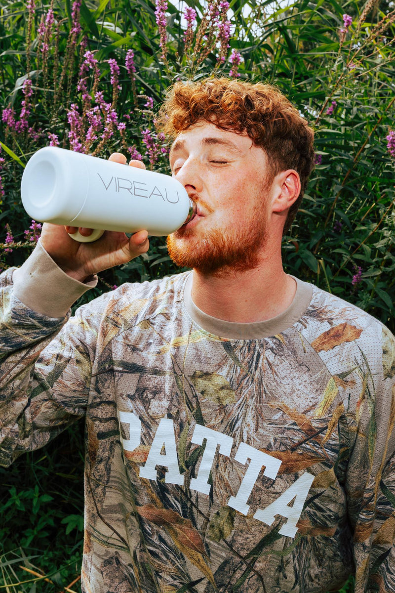 Man drinkt uit een witte Vireau RVS drinkfles in de natuur – duurzaam alternatief voor plastic flessen.